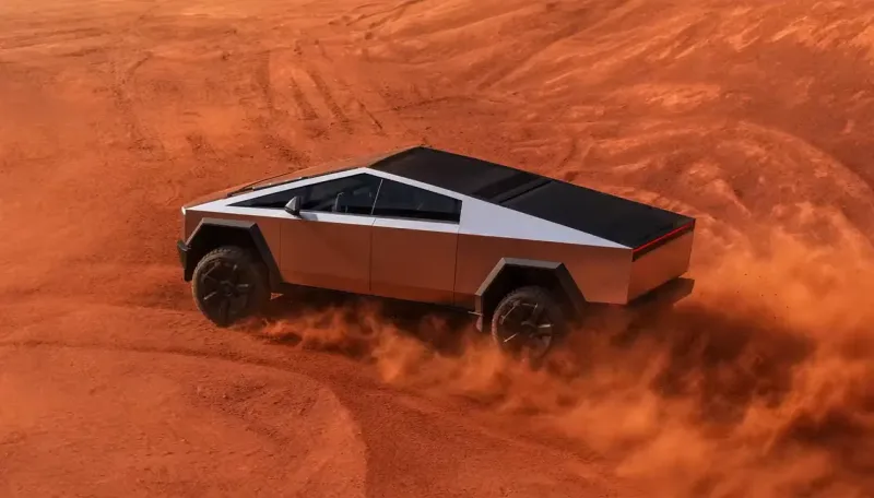An angular stainless steel pickup truck with a sharp wedge profile drives across rust red desert sand, seen from above, kicking up dust behind its rear wheels beside curving tire tracks.