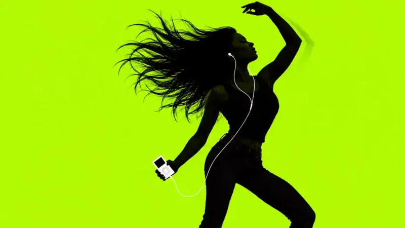 A black silhouette of a person with long spread hair, one arm raised, holding a small white device with white earbud cords, on lime green.